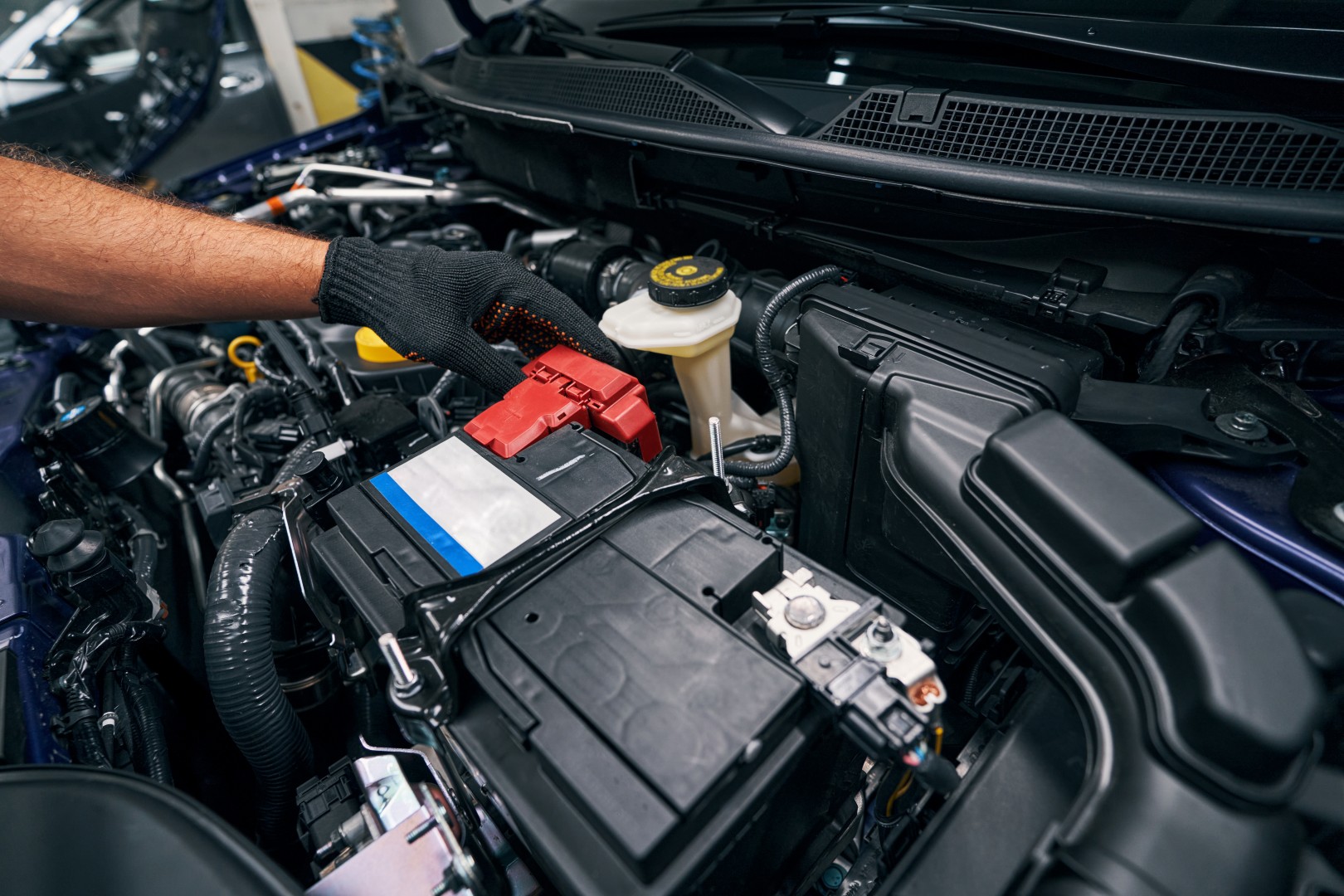 Repairman touching red battery inside an automobile with hand in glove during his maintenance inspection