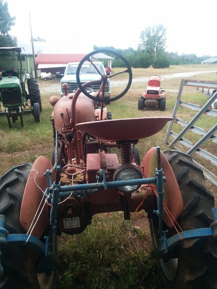 old tractor sitting in a field alongside other farm equipment and a truck